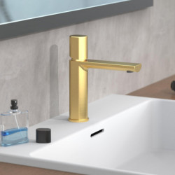 Goldfarbene Einhebelarmatur auf weißem Waschbecken vor grauer Wand.