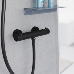 Schwarze Duscharmatur mit zwei Drehgriffen und angeschlossenem Duschschlauch an grauer Wand.