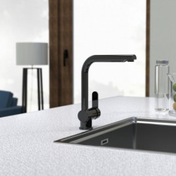 Schwarze Küchenarmatur mit eckigem Auslauf auf grauer Arbeitsplatte neben Spülbecken.